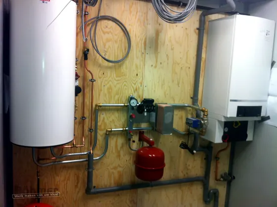Cv-ketel met boiler en leidingwerk op een houten installatiewand